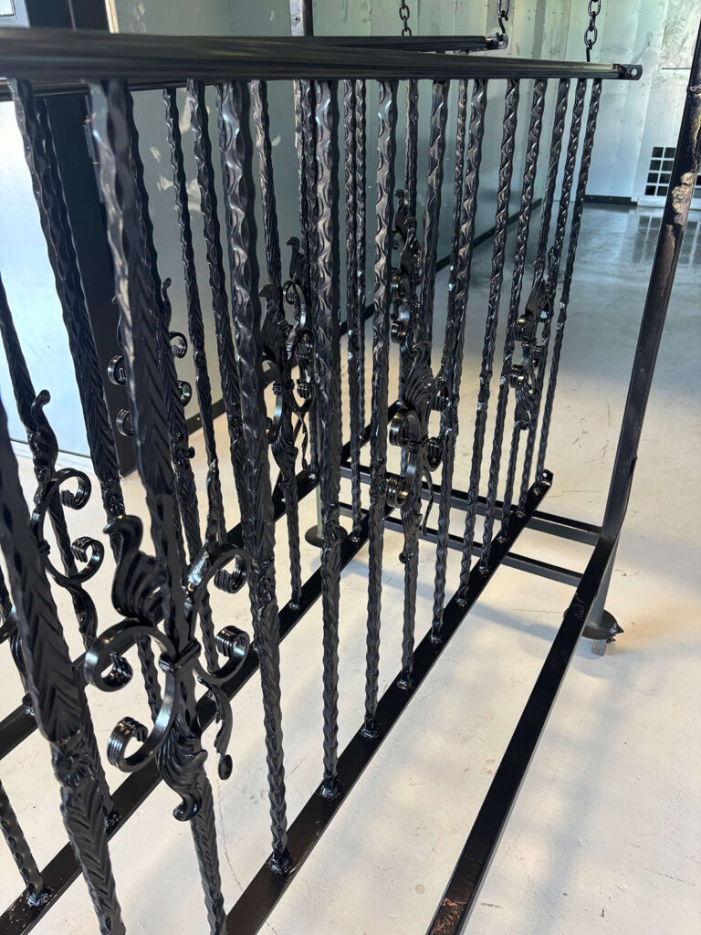 Finished glossy black powder-coated twisted-bar railing with scrolls, hanging on a shop rack.