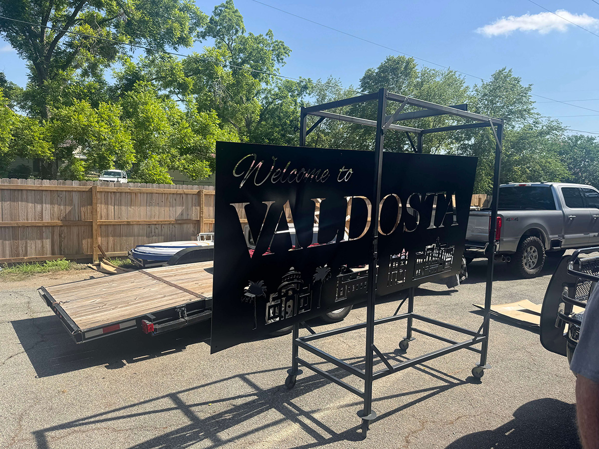 Large black Welcome to VALDOSTA cut-metal sign on a rolling rack in the yard.