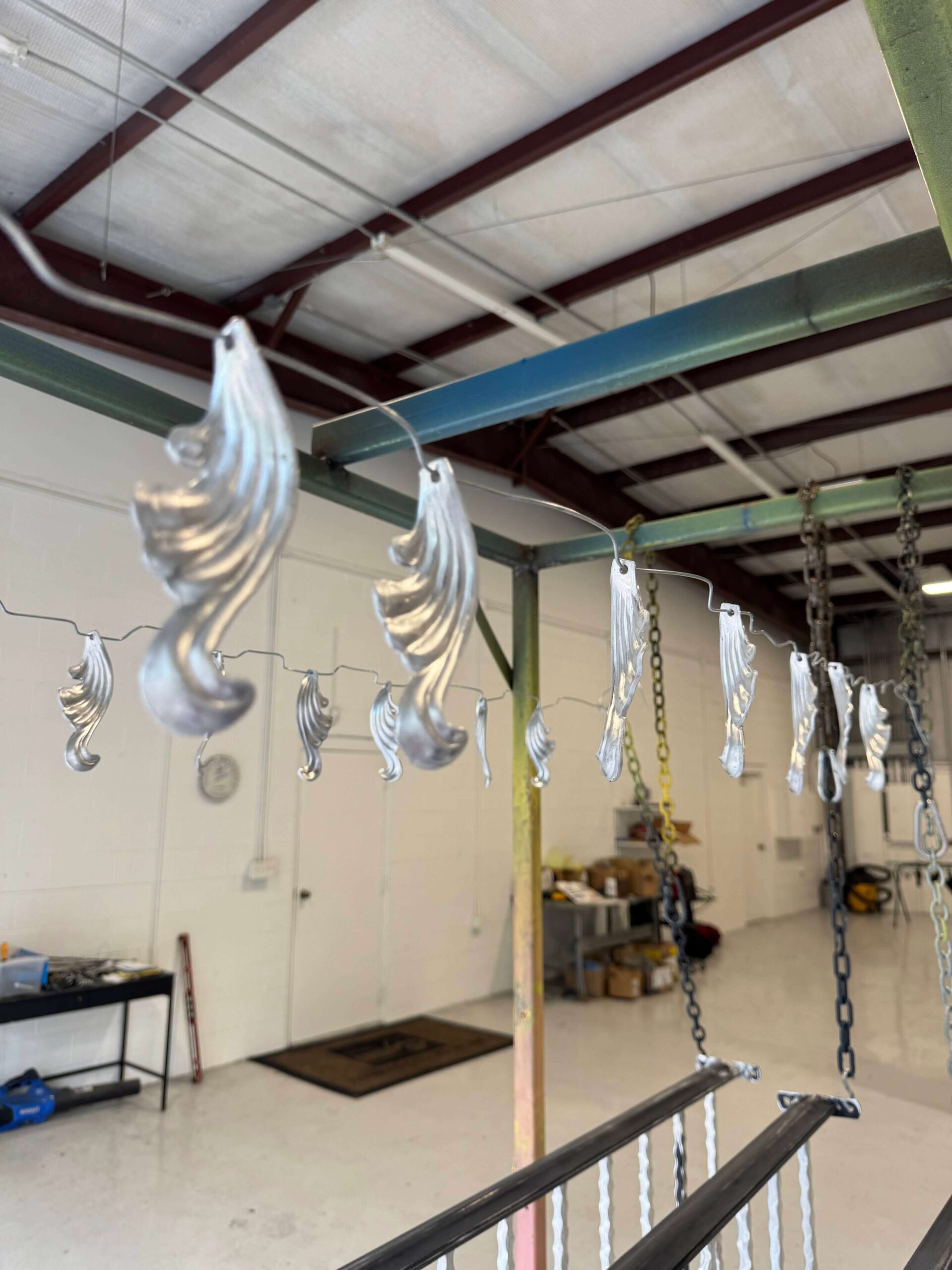 Shop interior: decorative scroll pieces hanging on wires from the ceiling, railing in the foreground.