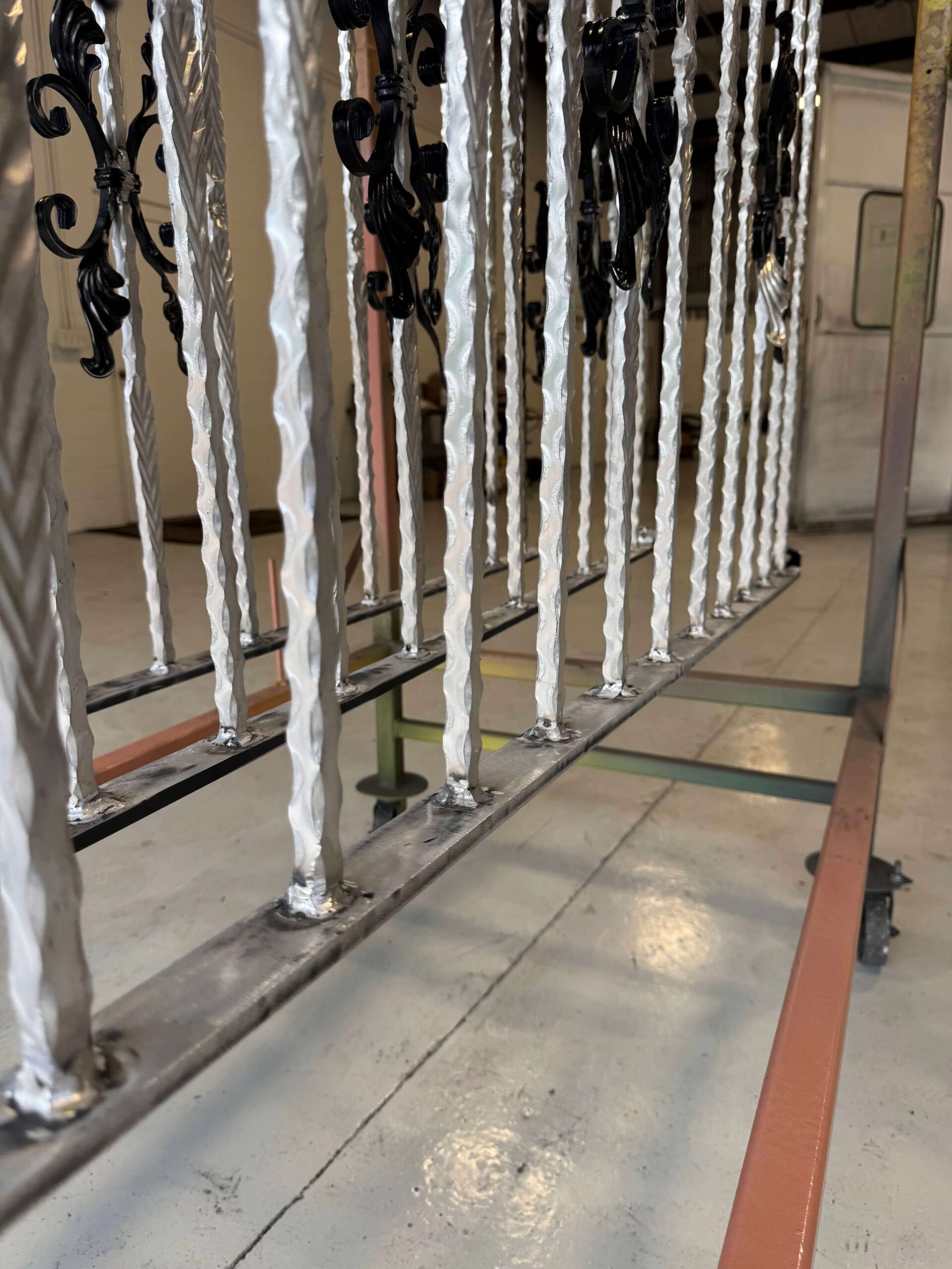 Close-up of a railing on a cart: twisted bars blasted silver, decorative scrolls already black.