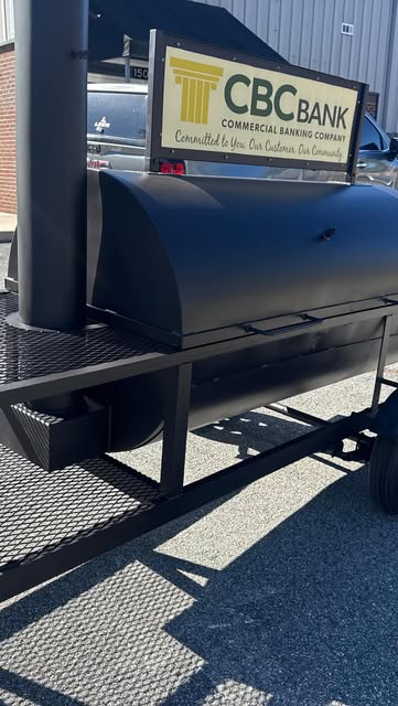 Satin-black powder-coated BBQ smoker trailer with a CBC Bank sign panel on it.